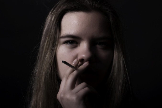 Teen girl smoking with black background: Smokedistrict Cannabis blog